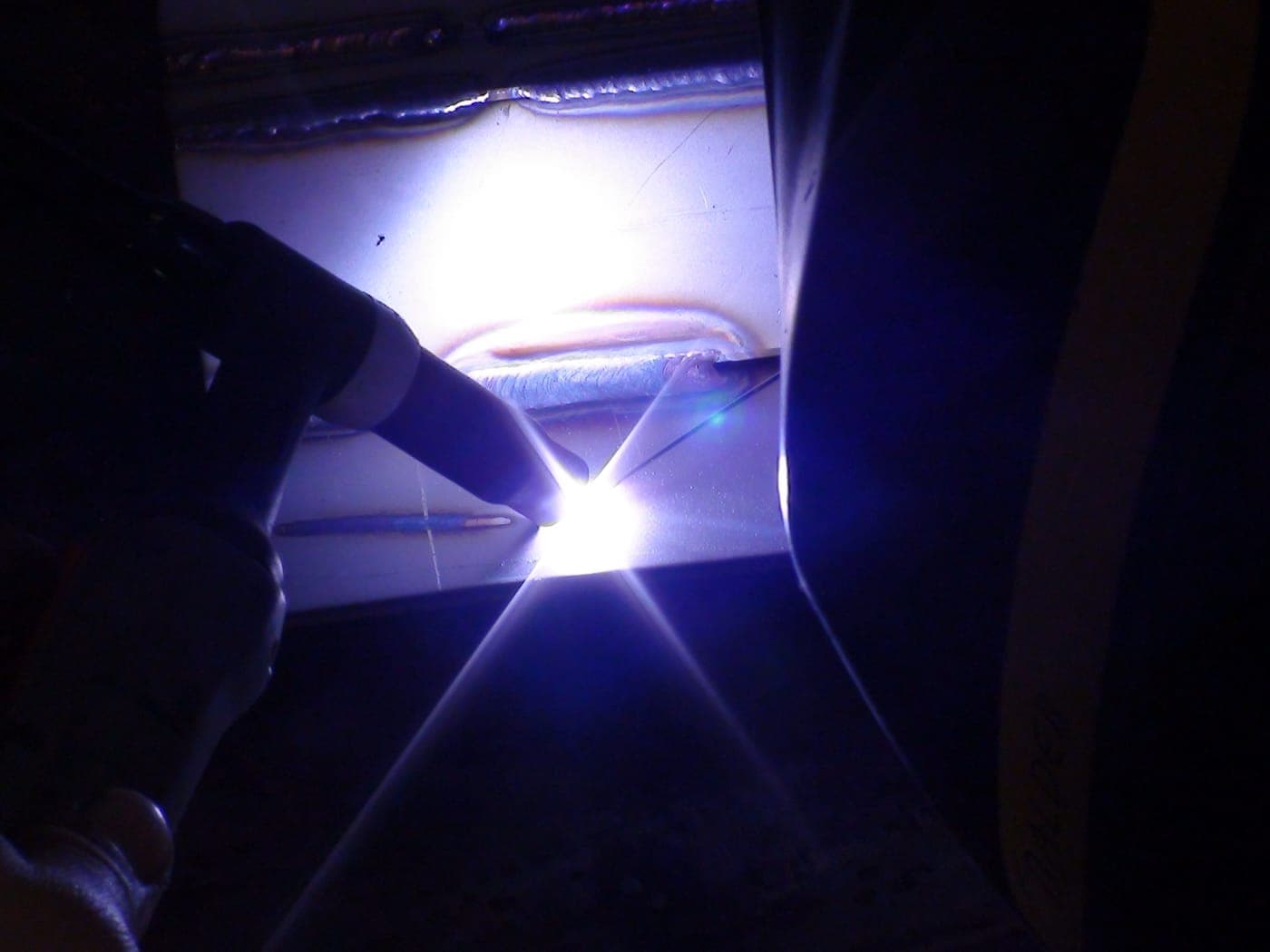Saldatore al lavoro con torcia TIG, scintille blu intense in ambiente industriale